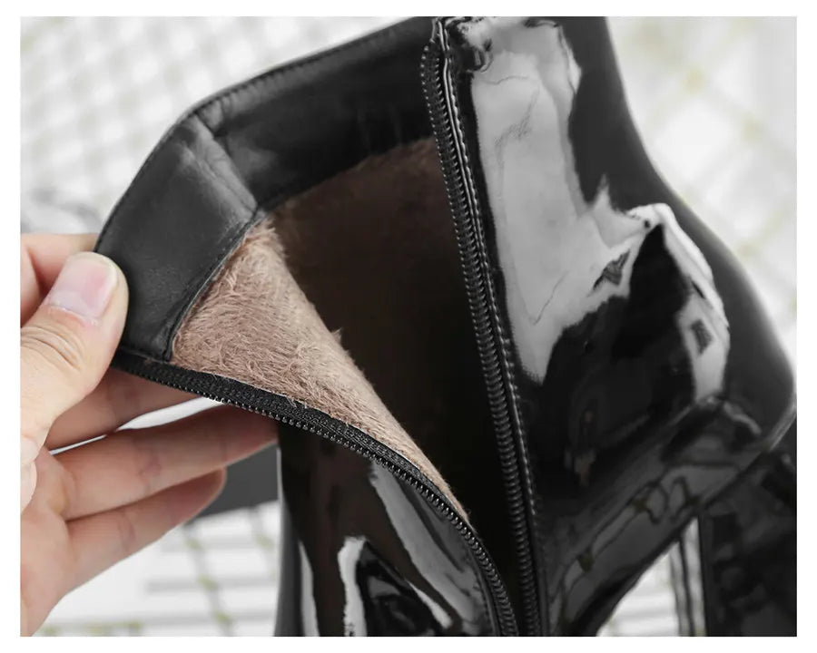 A close-up of a glossy black patent leather boot being held open by a hand, showing a brown faux-fur lining inside.