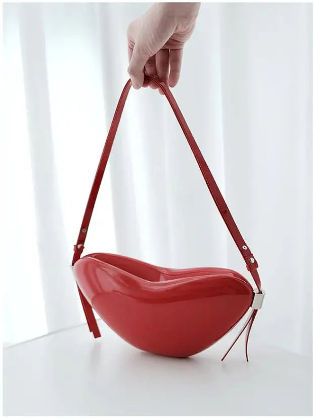 Red handbag with a strap held by a hand against a white background