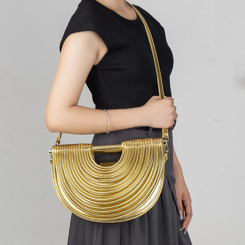 Gold handbag held by a person against a gray background