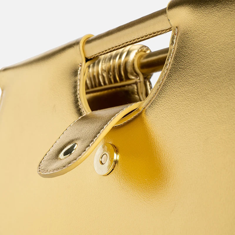 Close-up of a gold handbag with handle and clasp detail.