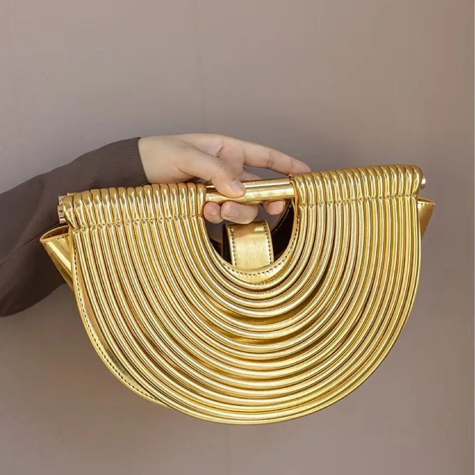 Gold handbag held by a hand against a plain background