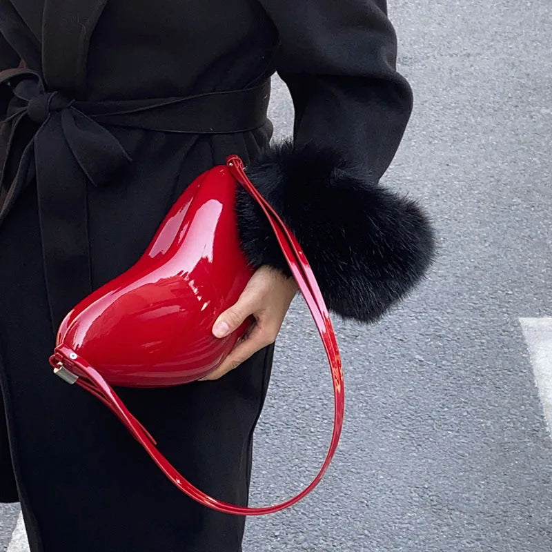 Person holding a red handbag with black fur trim on a gray pavement background